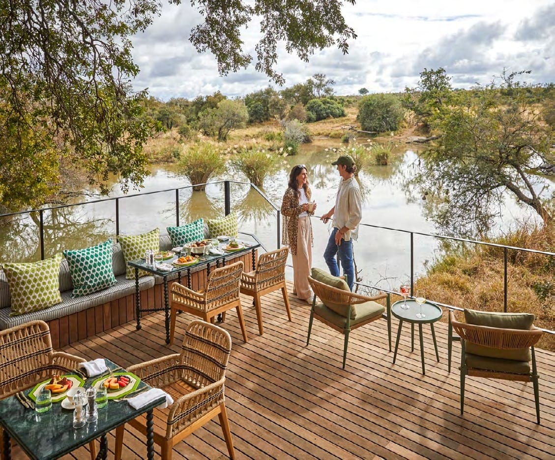 Guests on the raised dining deck at Malewane Lodge overlooking a waterhole in the Thornybush.