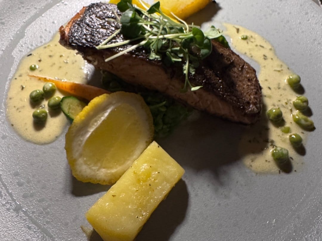 Pan-fried salmon with lemon, peas and potato on a grey plate at 18 On The Hill