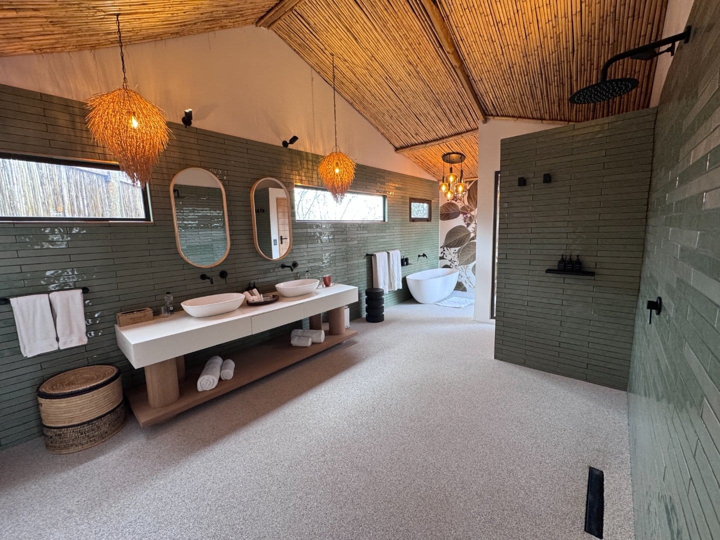 Tented suite bathroom with green tiled wall, twin basins, reed ceiling and a freestanding bath