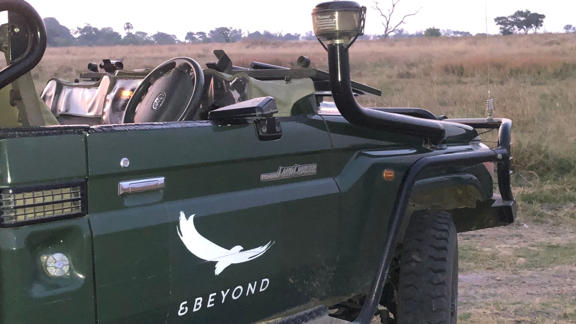 Open-sided game-drive vehicle parked on dry grassland at dusk in Botswana.