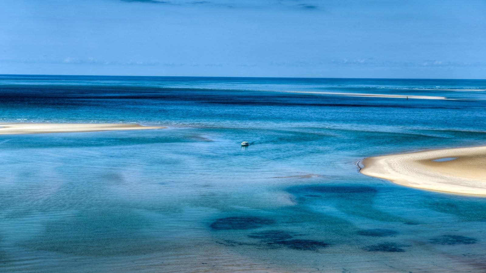 A small boat crossing turquoise shallows between white sandbanks on the Indian Ocean
