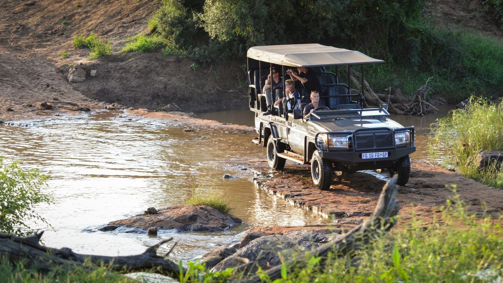 Open game vehicle crossing a shallow river in Madikwe in the late-afternoon light