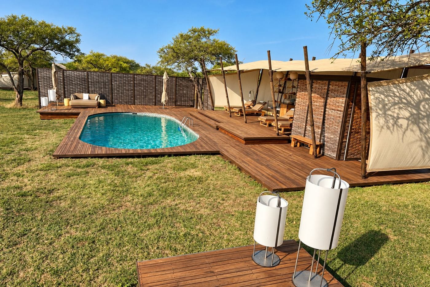 Plunge pool and timber deck beside canvas-walled suites on a grassy lawn under acacia trees