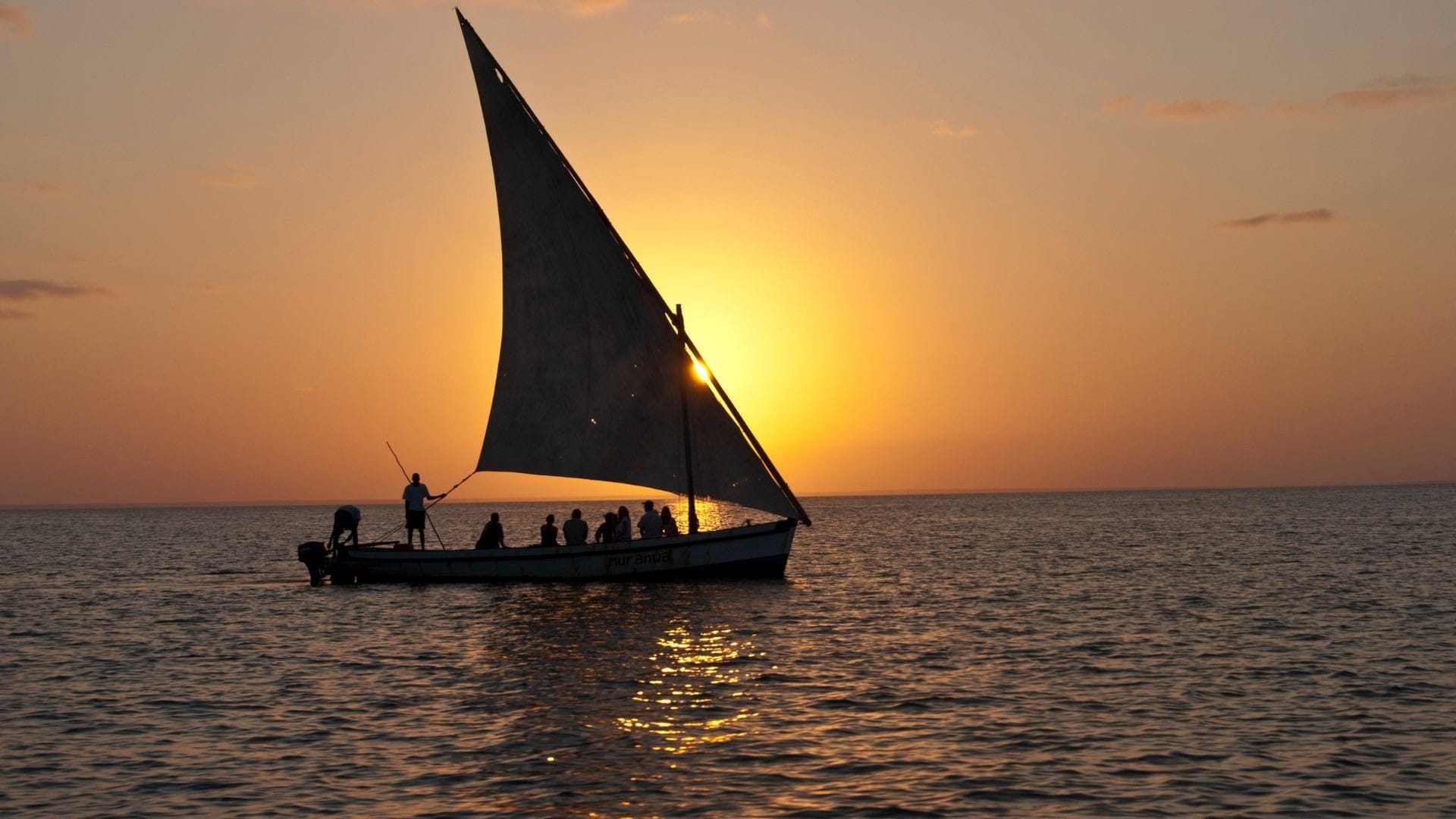 A dhow under full sail at sunset with guests aboard, the sun setting behind the sail on the Indian Ocean, Mozambique