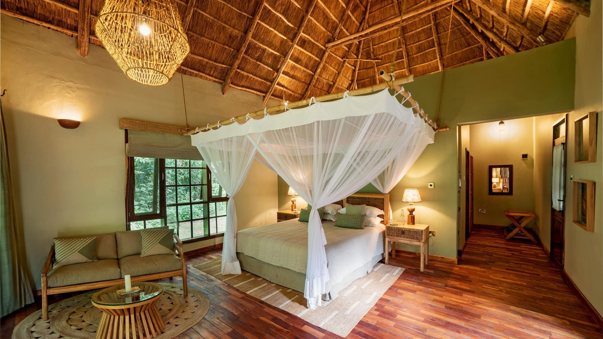 Thatched forest room with a four-poster bed and mosquito net looking onto the trees, Uganda