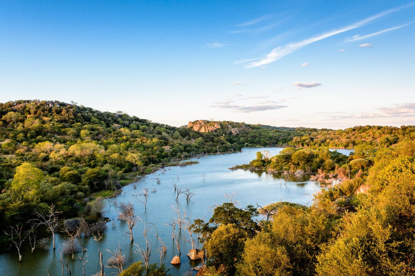 A wooded valley and flooded lake at golden hour in the private reserve of south-east Zimbabwe, granite outcrops on the far ridge