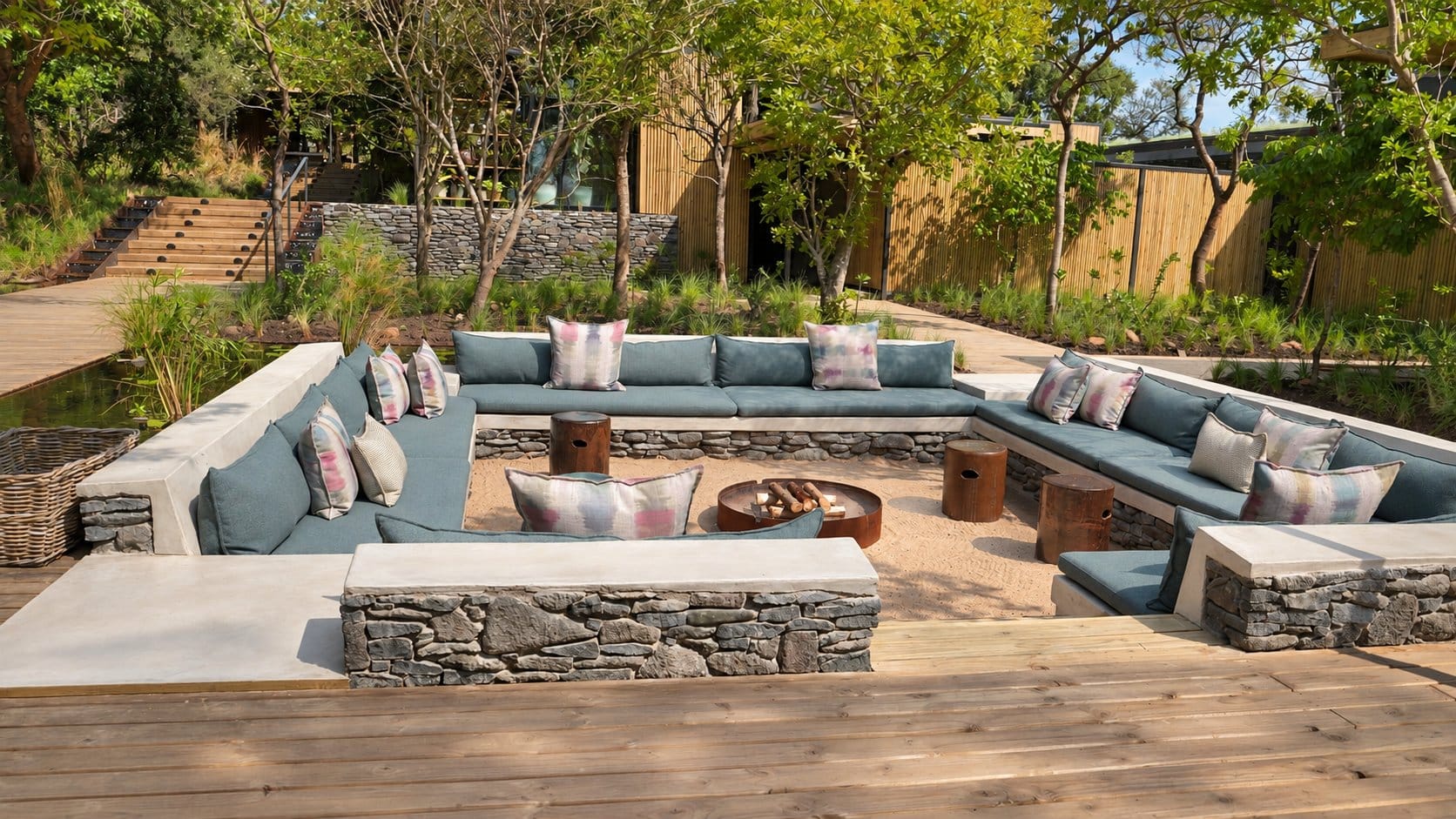 Sunken firepit lined with blue cushioned seating, set into a timber deck with garden steps behind