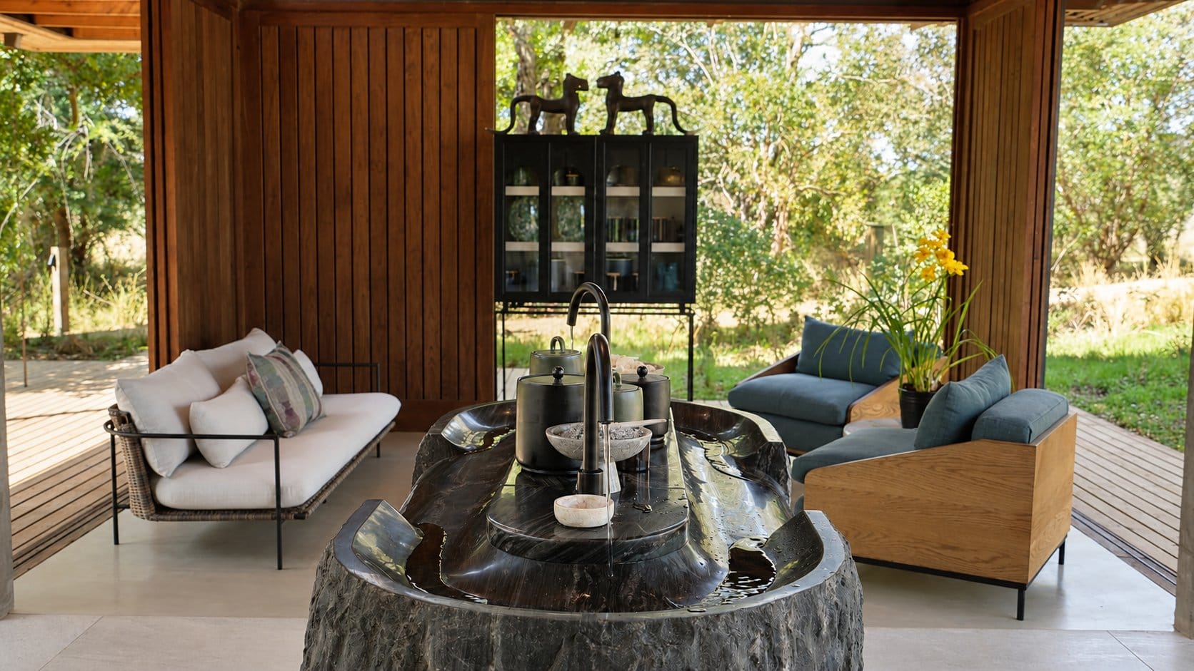 Open-sided entrance pavilion with a carved stone basin, a sofa and armchairs looking out to the bush