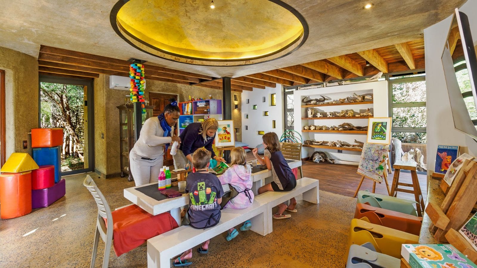 Children painting at a table in a bright lodge activity room, with skulls and bush finds on the shelves behind