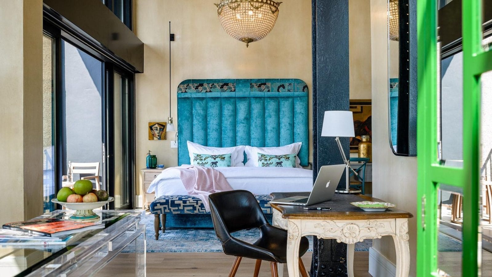 Hotel suite in Cape Town with a teal velvet headboard, crystal chandelier and a writing desk by the window