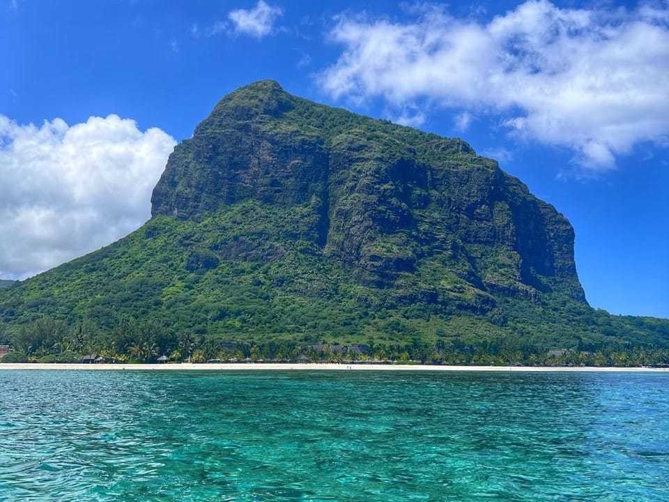 Turquoise lagoon water in front of a steep green mountain and white sand beach in Mauritius
