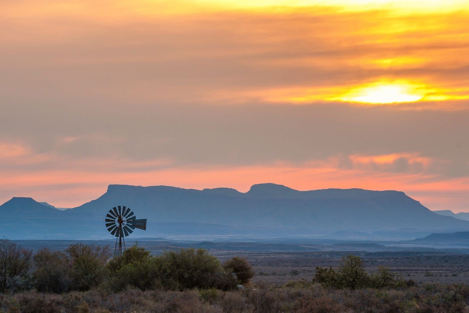 Windmill silhouetted against flat-topped Karoo mountains at sunset