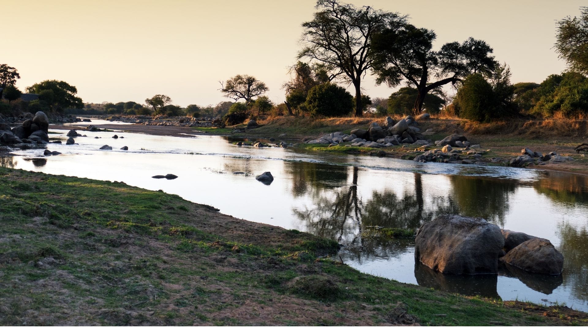 A southern Tanzanian river at first light, boulders and acacia along the bank