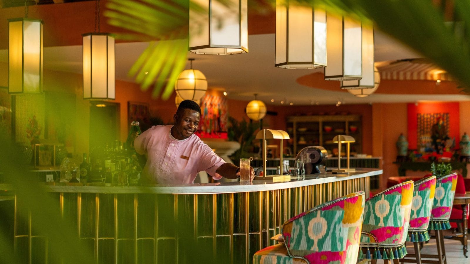 Smiling barman preparing a drink at a colourful lodge bar under paper lanterns