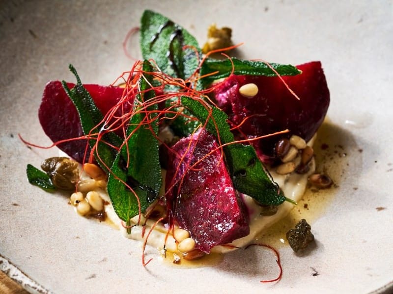 Plated roasted beetroot with crisp sage leaves, pine nuts and a light purée on a handmade ceramic dish