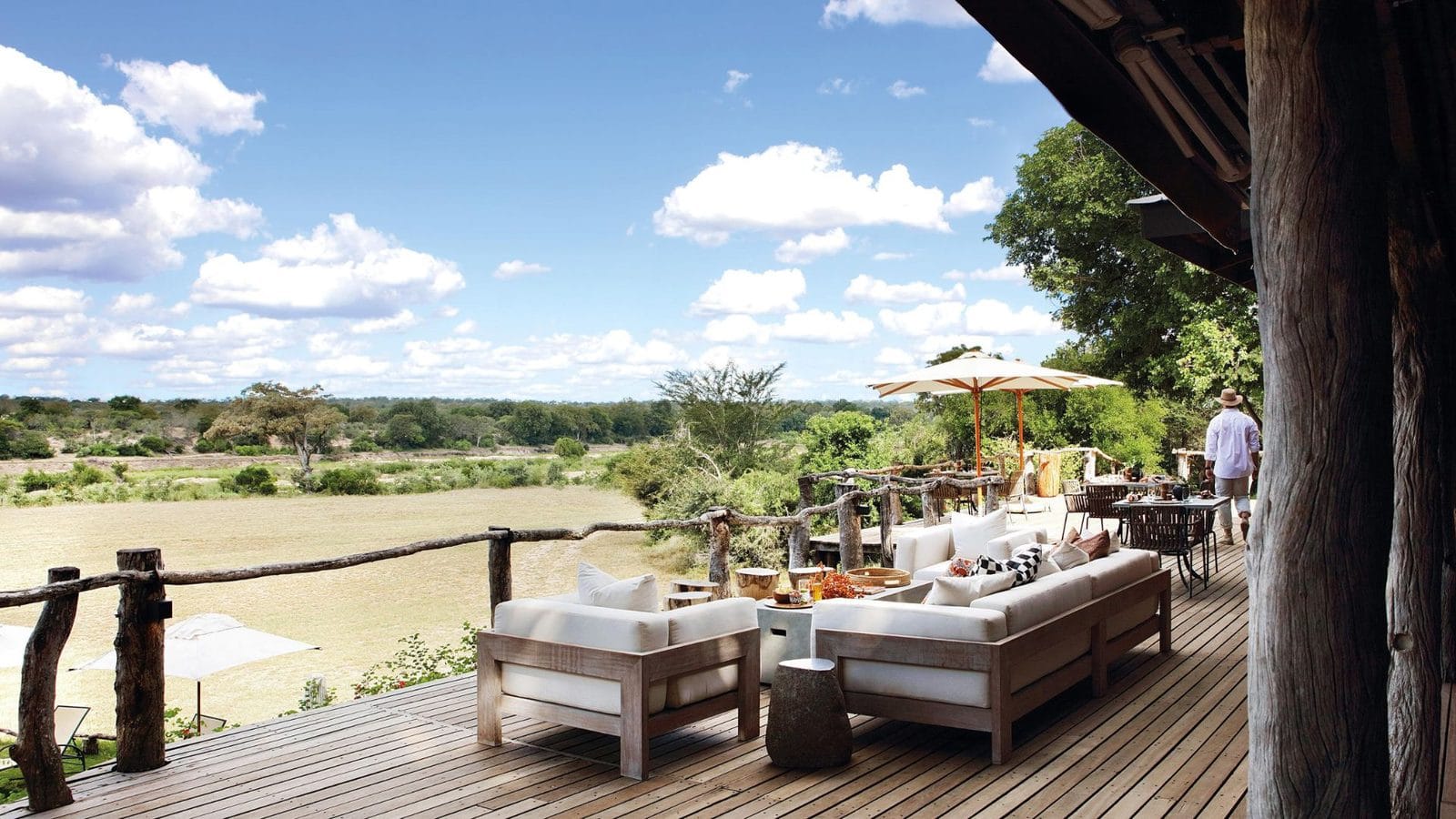 Wide, level timber deck with sofas and umbrellas overlooking a riverbed and the bushveld beyond