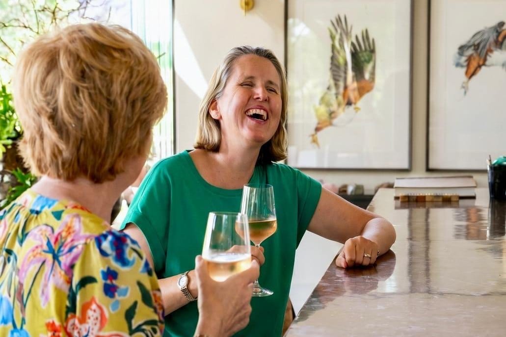 Vikki and Sian laughing over glasses of white wine at a tasting counter in the Cape Winelands