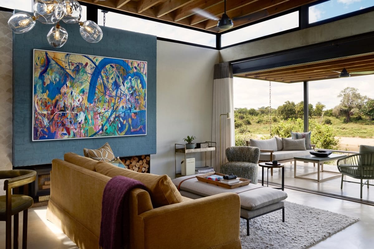Safari suite lounge with a large abstract painting, a mustard sofa and doors open onto a riverside deck