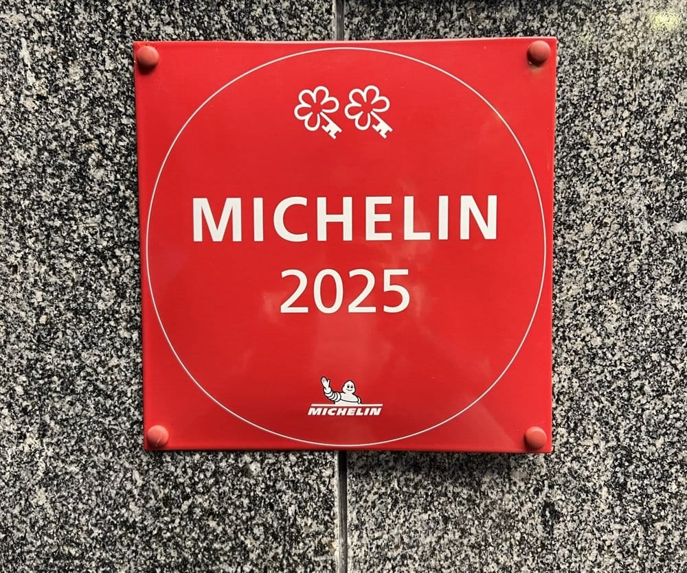 Red Michelin plaque with two keys and the year 2025, mounted on a granite wall outside a hotel