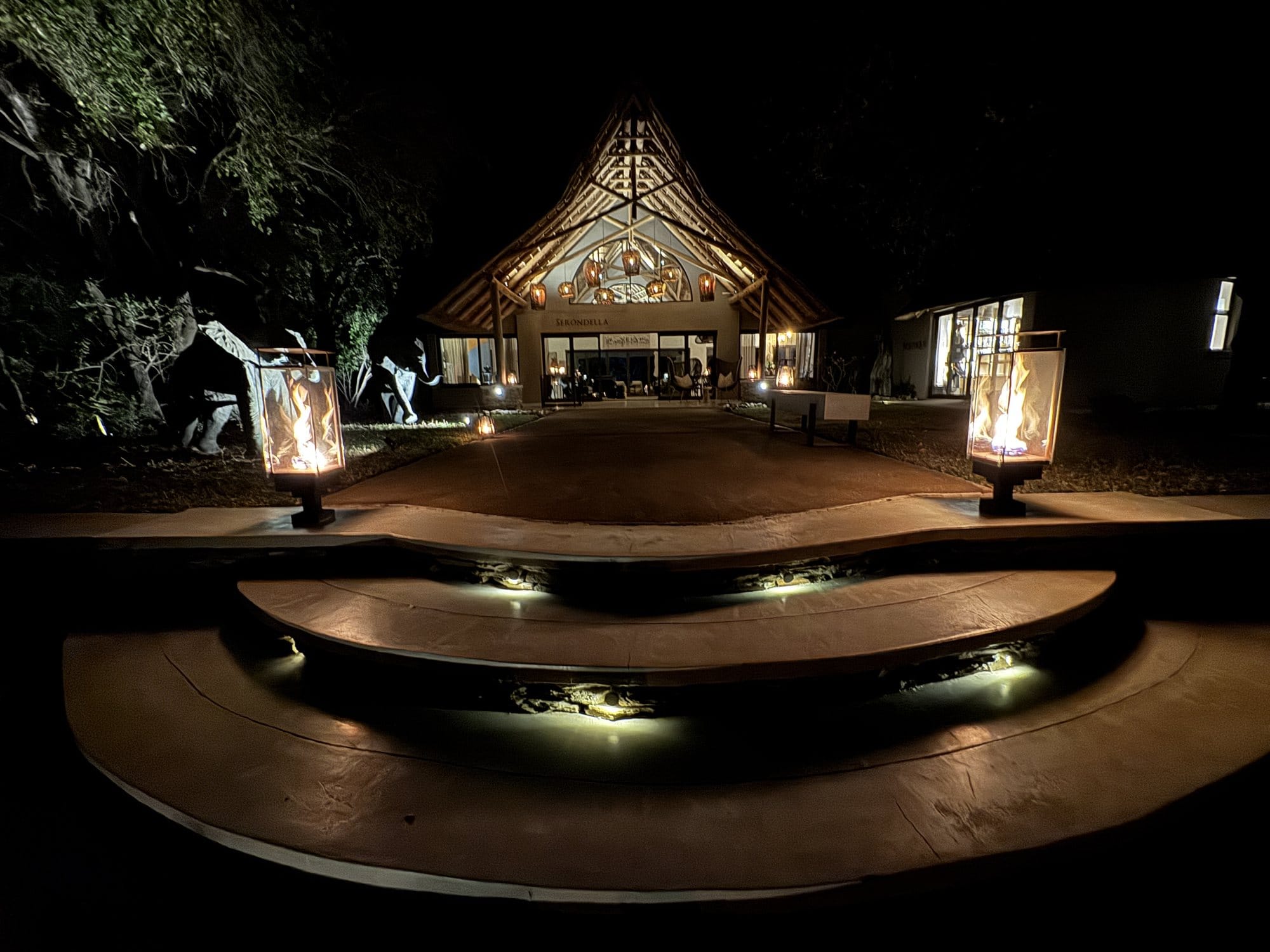 Serondella's thatched main lodge entrance at night, lit by lanterns