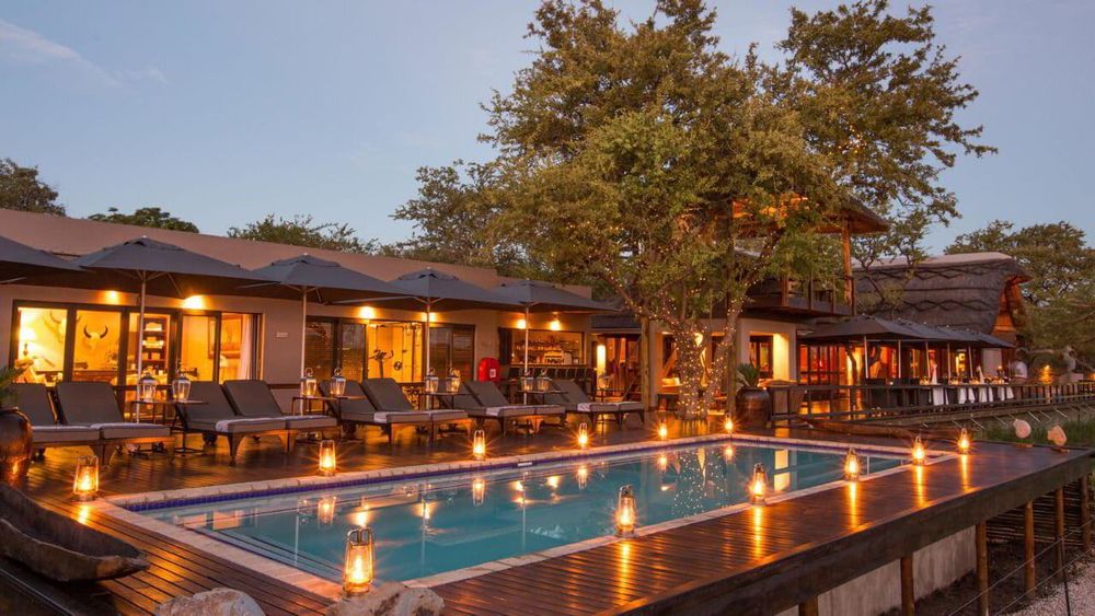 A luxury safari lodge at night with lanterns around the pool