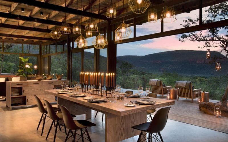Lantern-lit outdoor dinner table set in the African bush at dusk