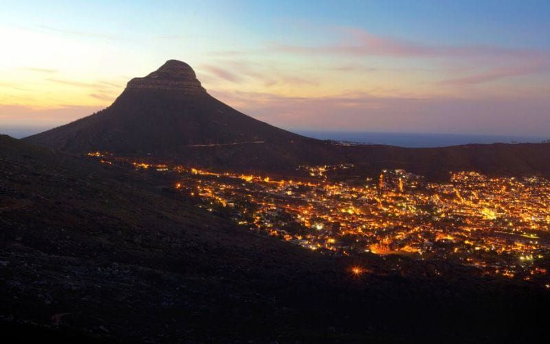Cape Town at sunset with Lion's Head silhouetted against a warm orange sky and the Atlantic below