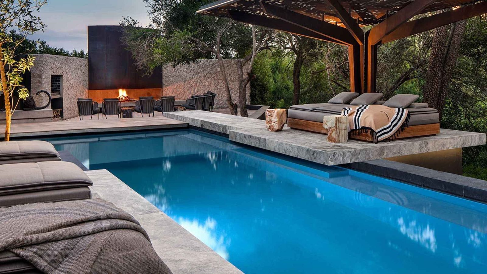 Private safari villa at dusk with pool and bush view, lights on in the lounge