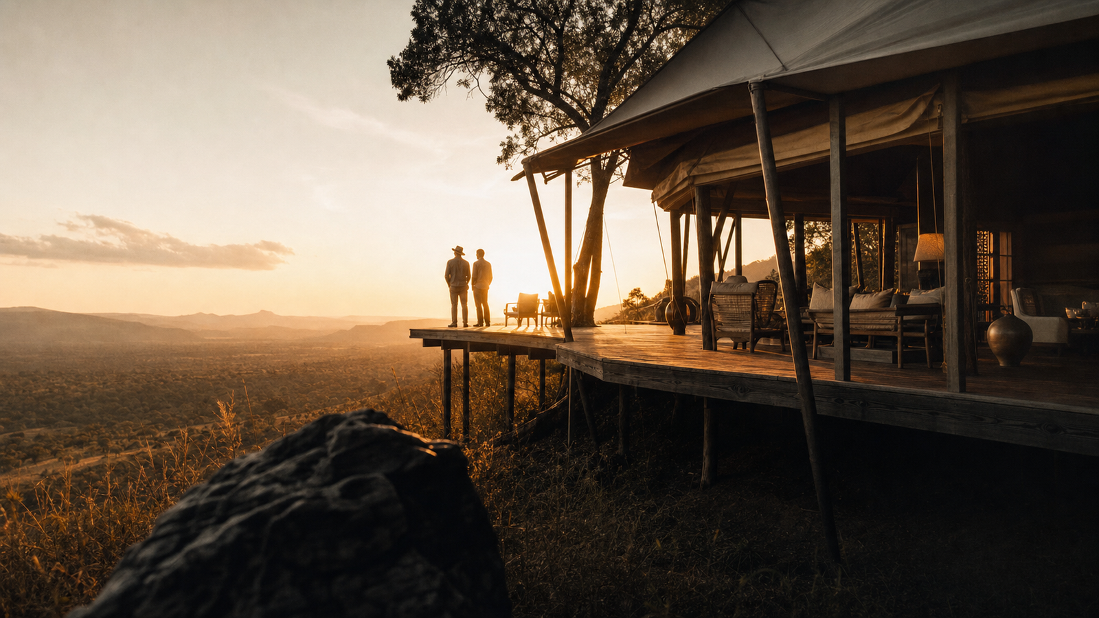 Two guests on a lodge deck at golden hour, looking out over an open African valley