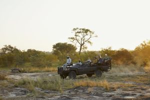 Guests on a stationary Cheetah Plains game drive vehicle in the Sabi Sand, golden light and dust behind them