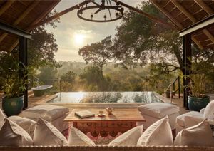 Thatched suite deck at Malewane Lodge at sunrise, with plunge pool, freestanding bath and wrought-iron chandelier overlooking the bushveld.