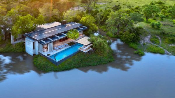 Aerial view of a luxury private safari villa beside a river in Africa, the kind of exclusive-use property that suits multi-generational family travel.