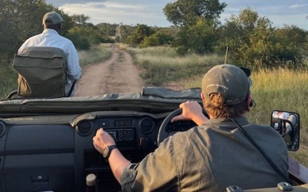 A qualified guide and tracker scanning the bush from an open game drive vehicle in South Africa, mid-morning light over dry savannah