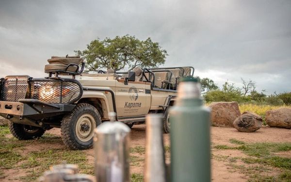 Guests at a bush drinks stop in the Kapama Private Game Reserve at golden hour, drinks in hand with open savannah behind them