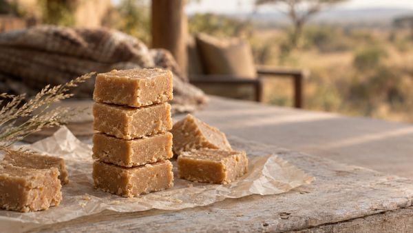 A stack of light caramel fudge squares on baking paper on a wooden table
