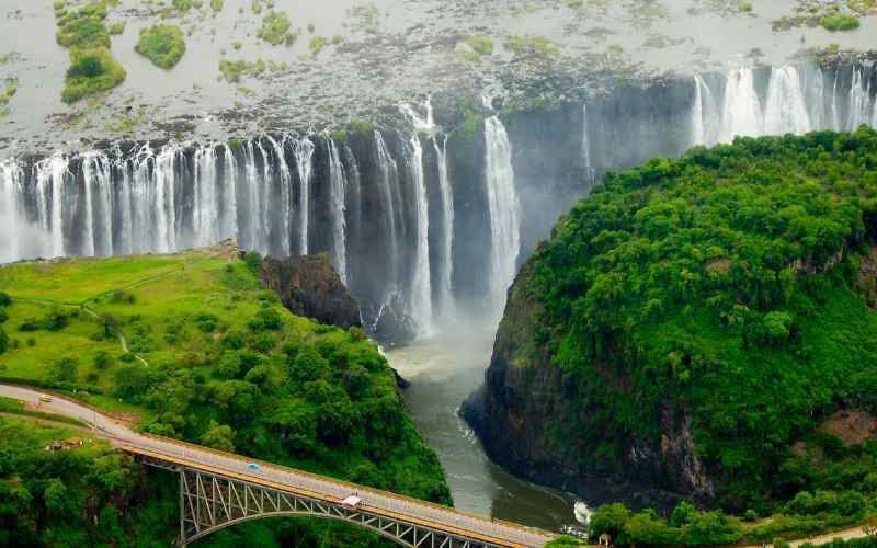 Aerial view of Victoria Falls cascading into the Batoka Gorge, surrounded by lush greenery and the iconic Victoria Falls Bridge—featured in a luxury solo safari in Africa itinerary.