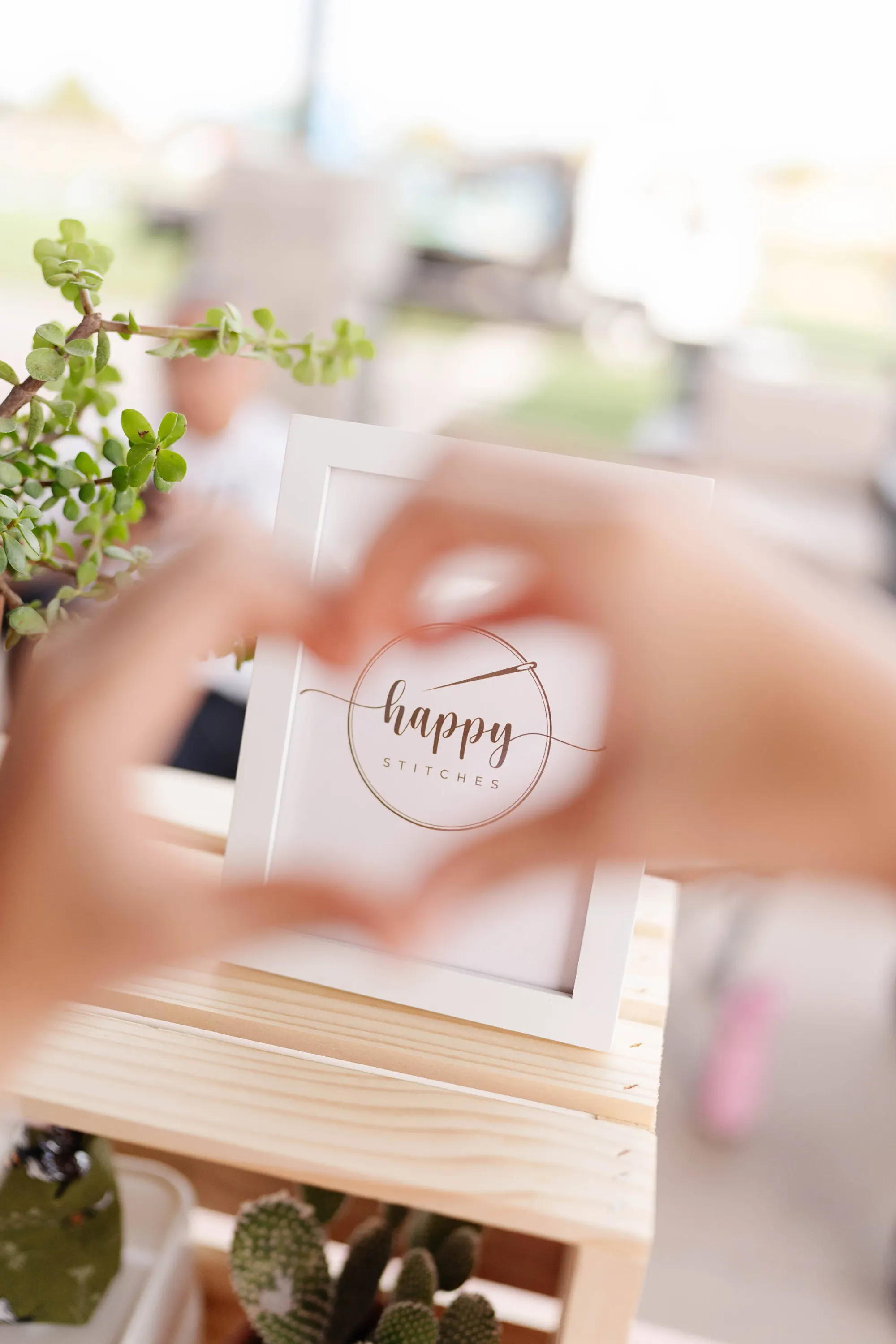 Happy stitches heart hands in front of logo