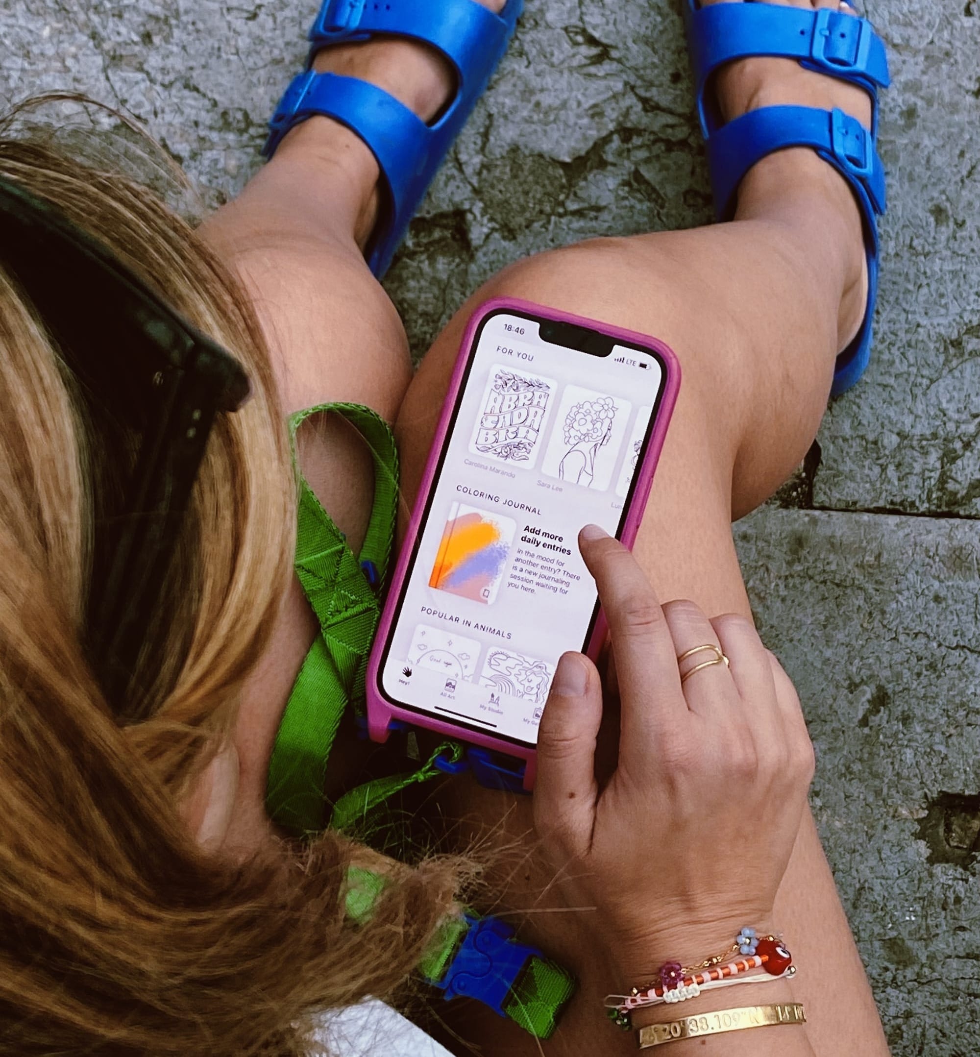 A person sitting on stairs, using their finger to color a digital illustration on the Lake app on an iPhone.