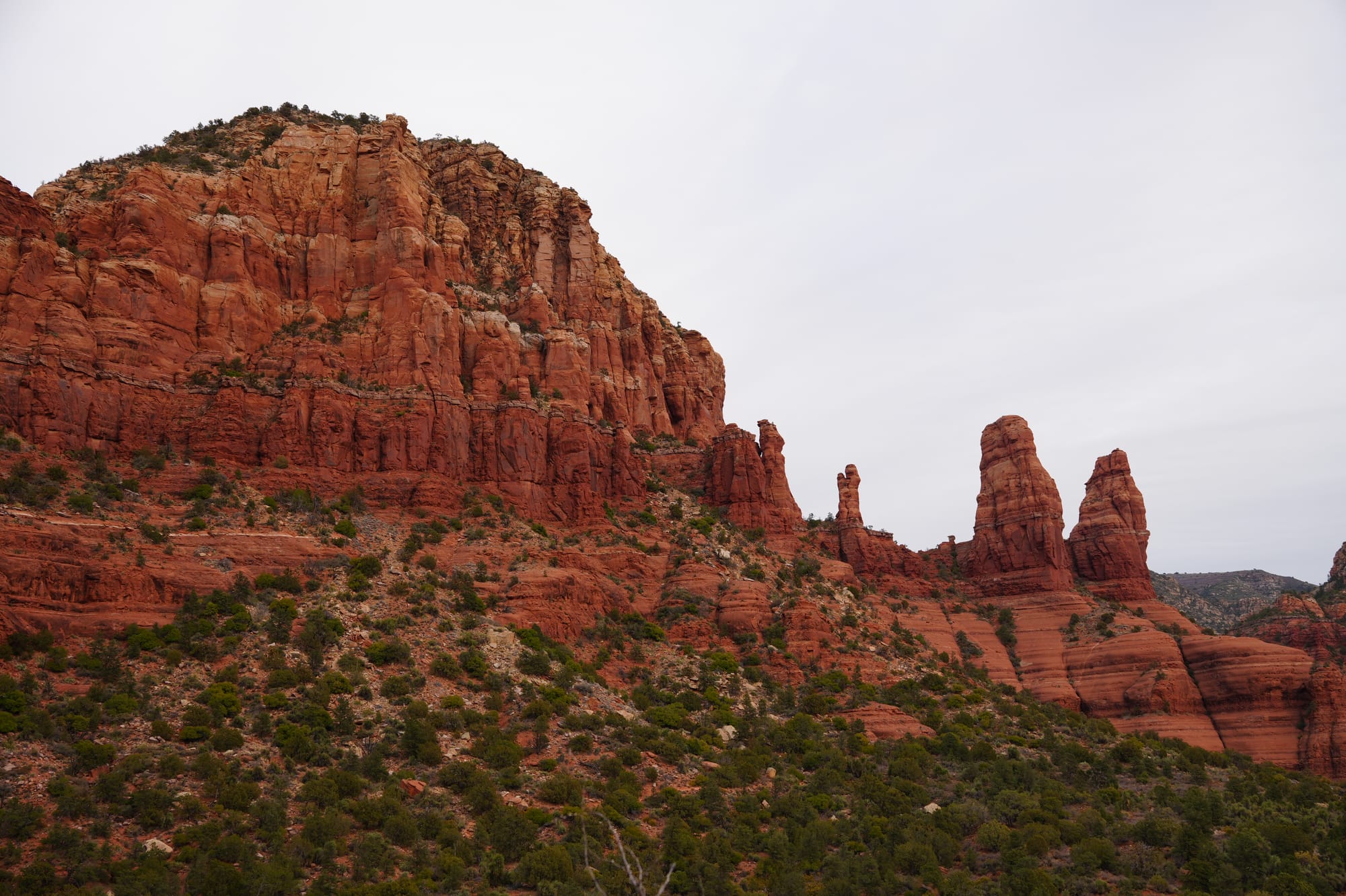 Landscape of the Sedona red rock formations with green shrubbery at the base against a clear sky.
