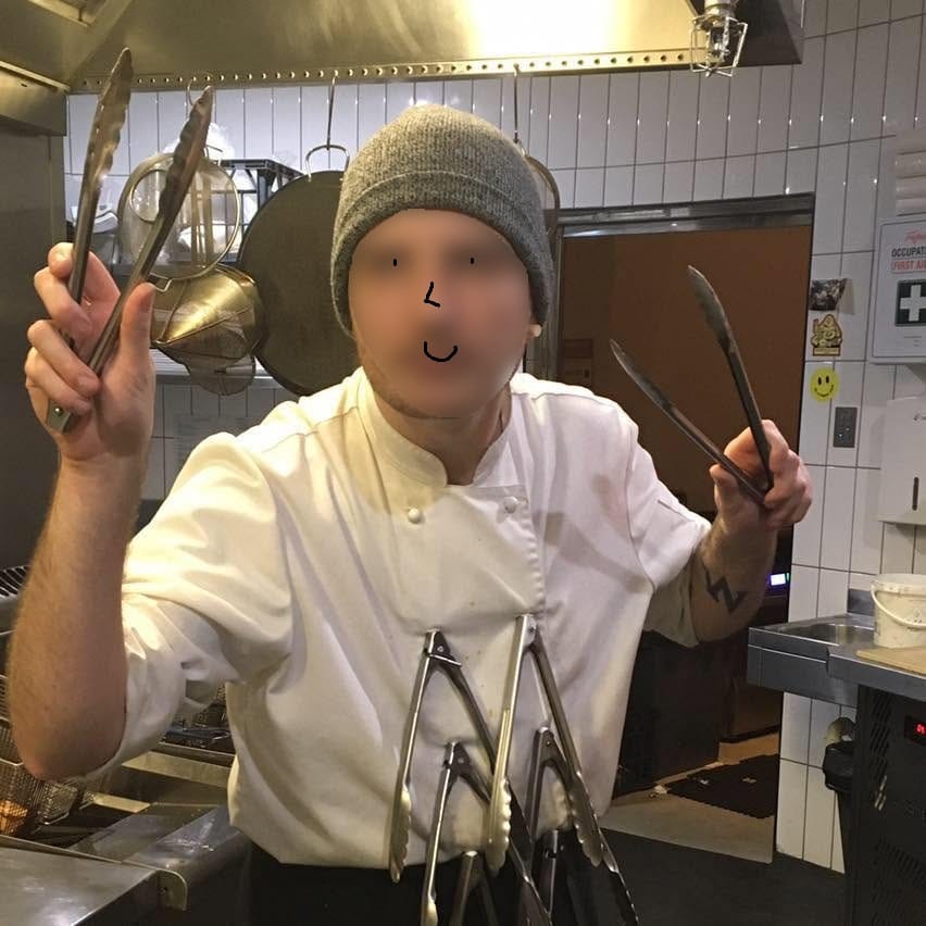 An image of a man in a chefs outfit. They have pairs of tongs clipped to the buttons on their jacket