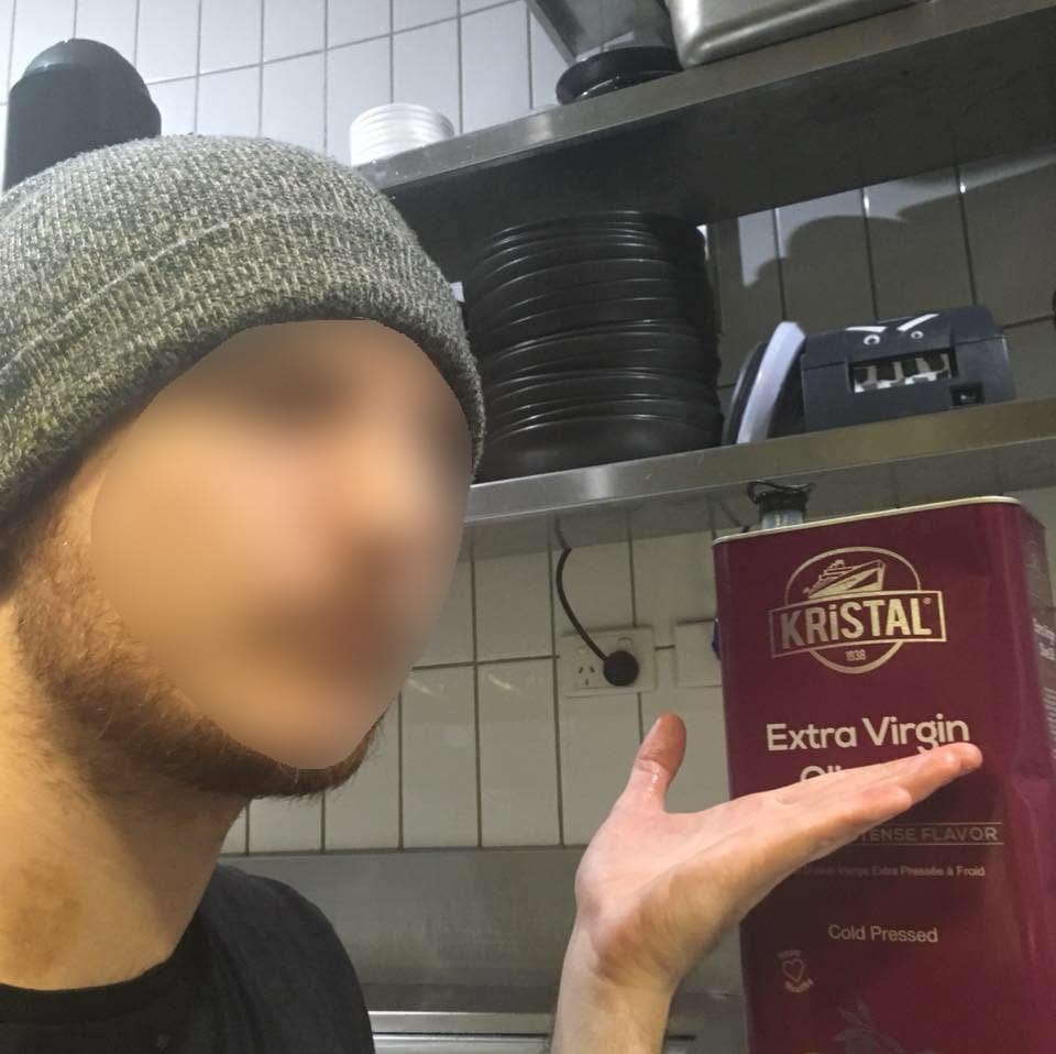 A man holds their hand up to a tin box of extra virgin olive oil, highlighting the 'Extra Virgin' part
