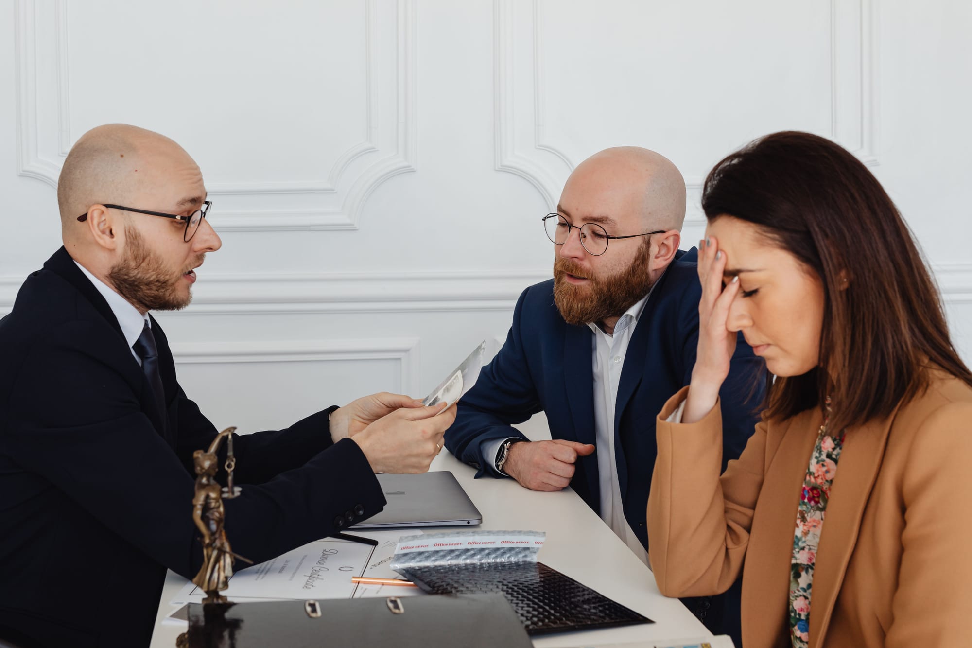 A lawyer reads a piece of paper to two clients. One of the clients looks upset