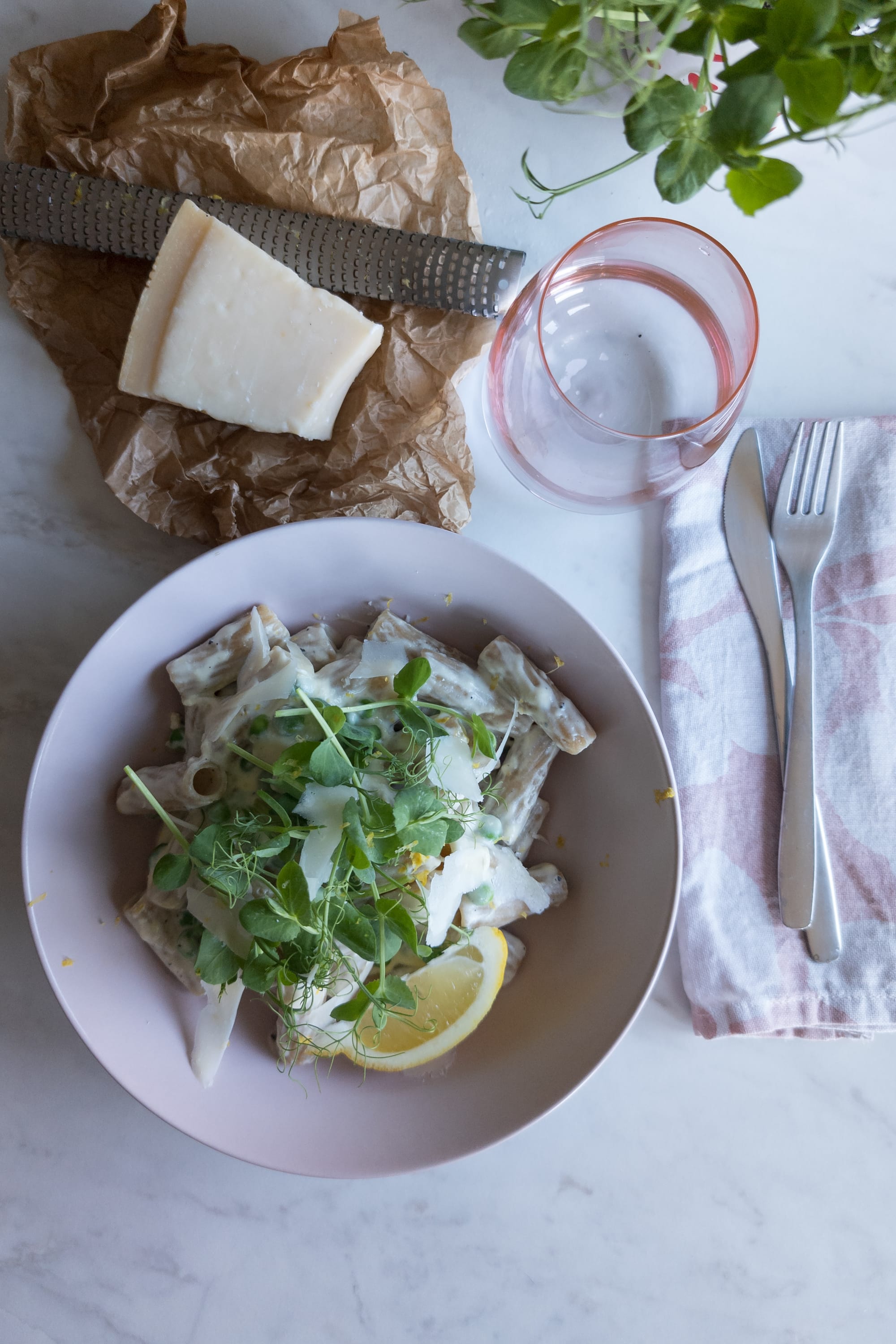 Schüssel mit Vollkornnudeln, Erbsen-Ricotta-Soße, garniert mit Erbsensprossen, Parmesan und Zitrone
