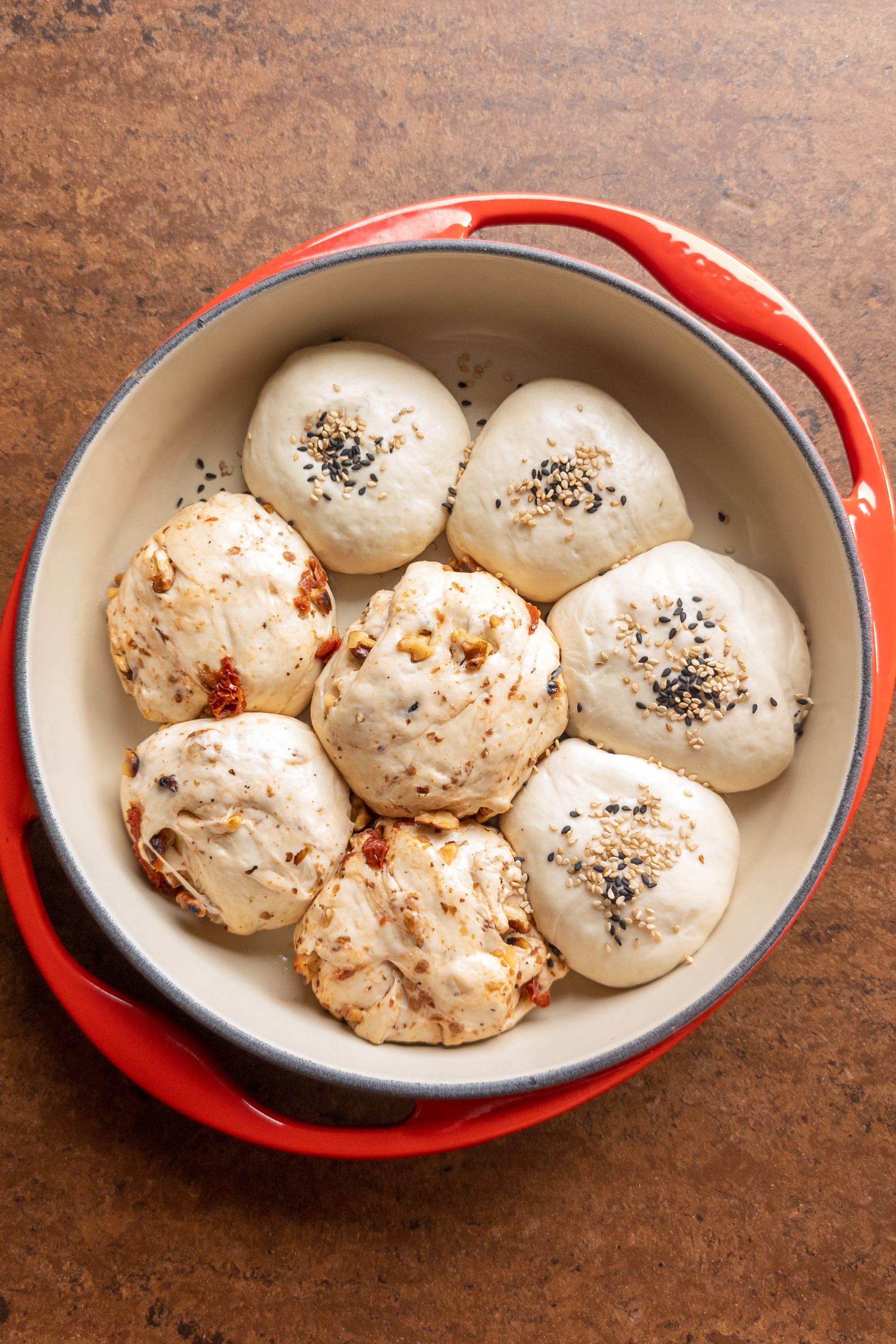 Teiglinge von zweierlei Dinkelbrötchen. Eine klassische Variante mit Sesam bestreut und eine Variante mit Walnüssen und getrockneten Tomaten