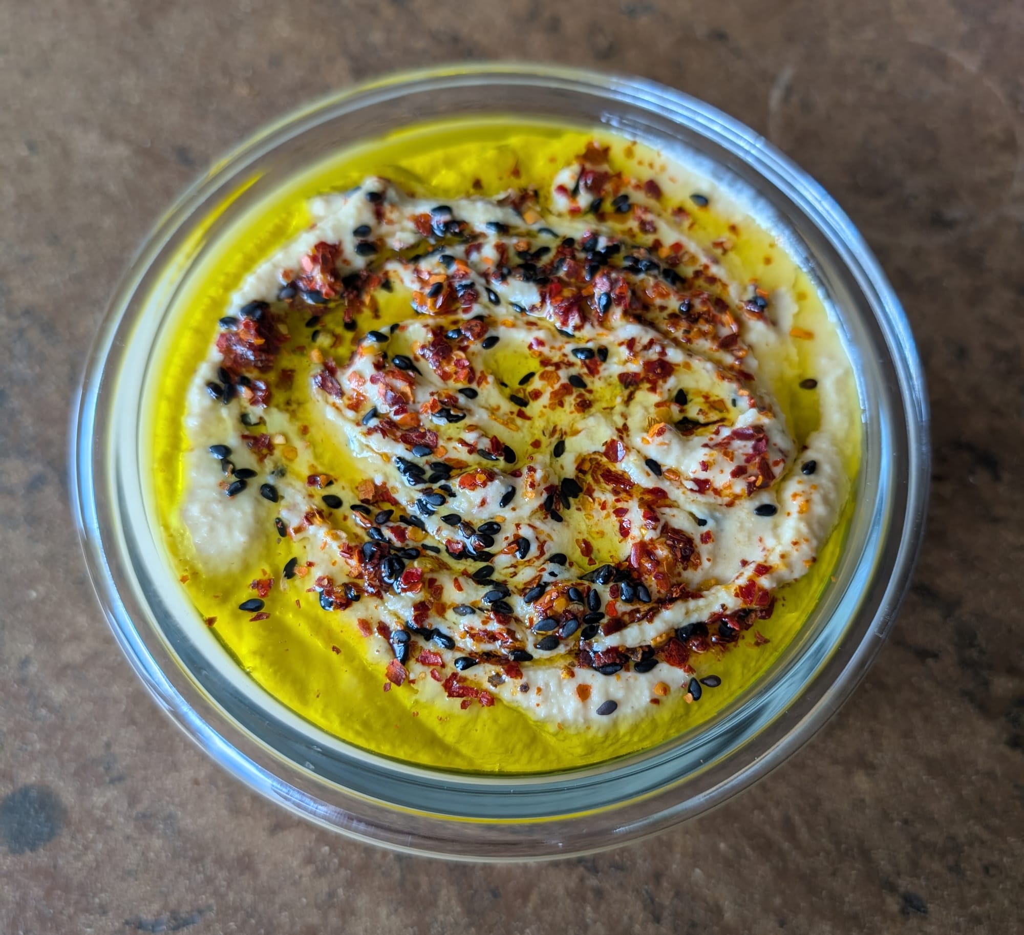 Eine Schale mit cremigem Hummus garniert mit Olivenöl, Chiliflocken und schwarzen und weißen Sesam
