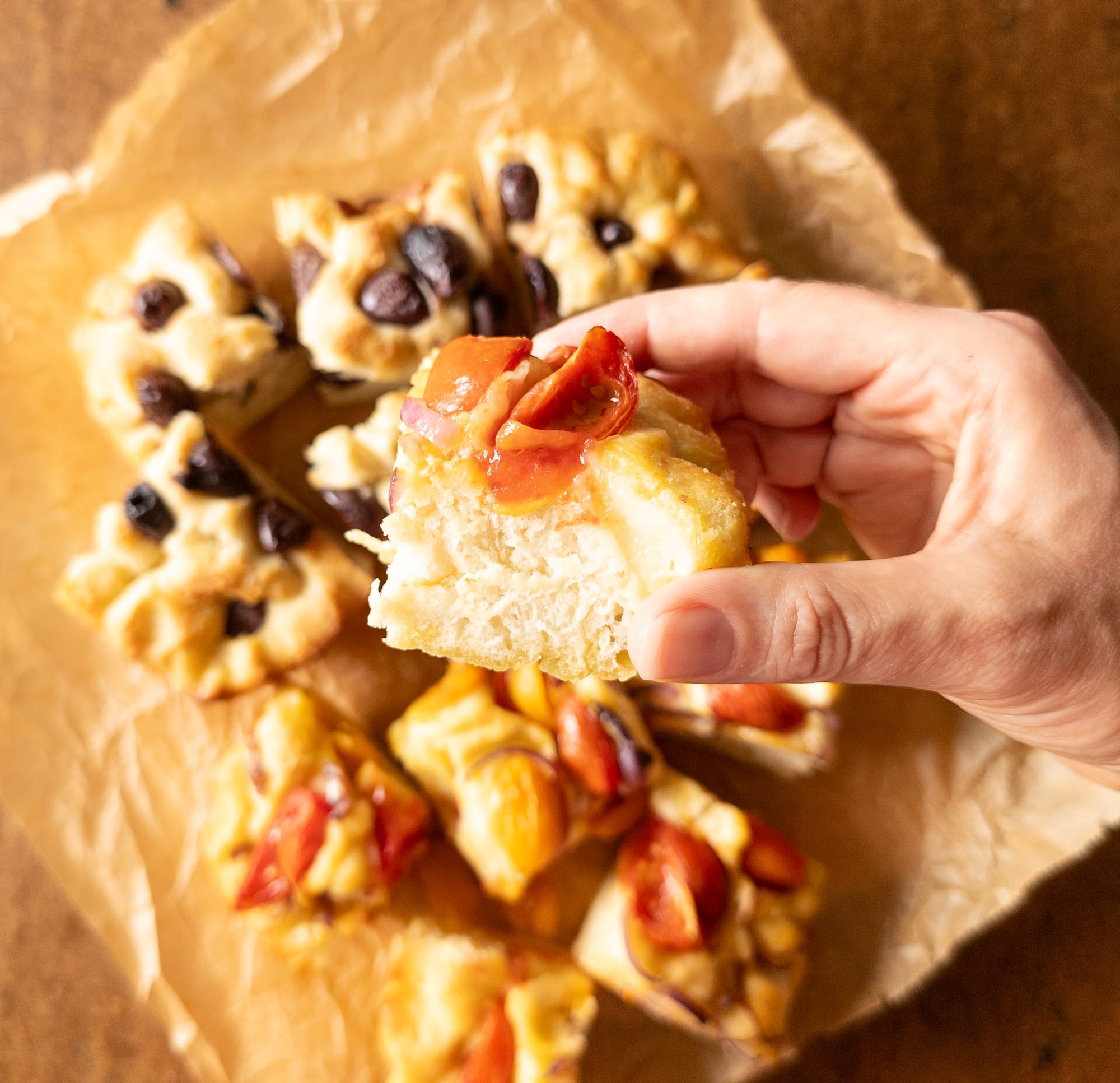 Ein Stück Focaccia mit Cherrytomaten und roten Zwiebeln in der Hand gehalten.
