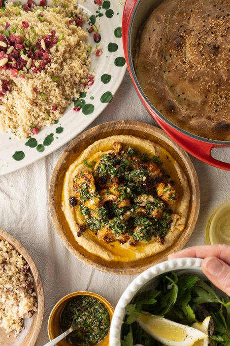 Eine Schüssel mit Hummus, darauf gerösteter Blumenkohl und Gremolata. Daneben Couscoussalat und Fladenbrot.