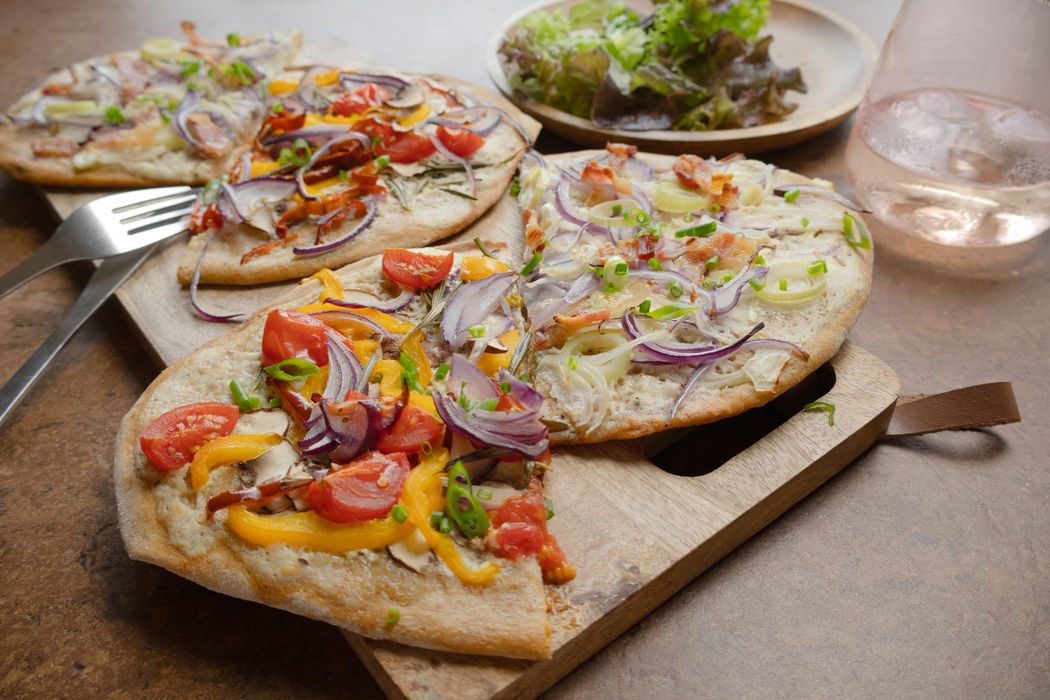 Zweierlei Flammkuchen belegt mit Gemüse und Speck auf Holzbrett angerichtet. 