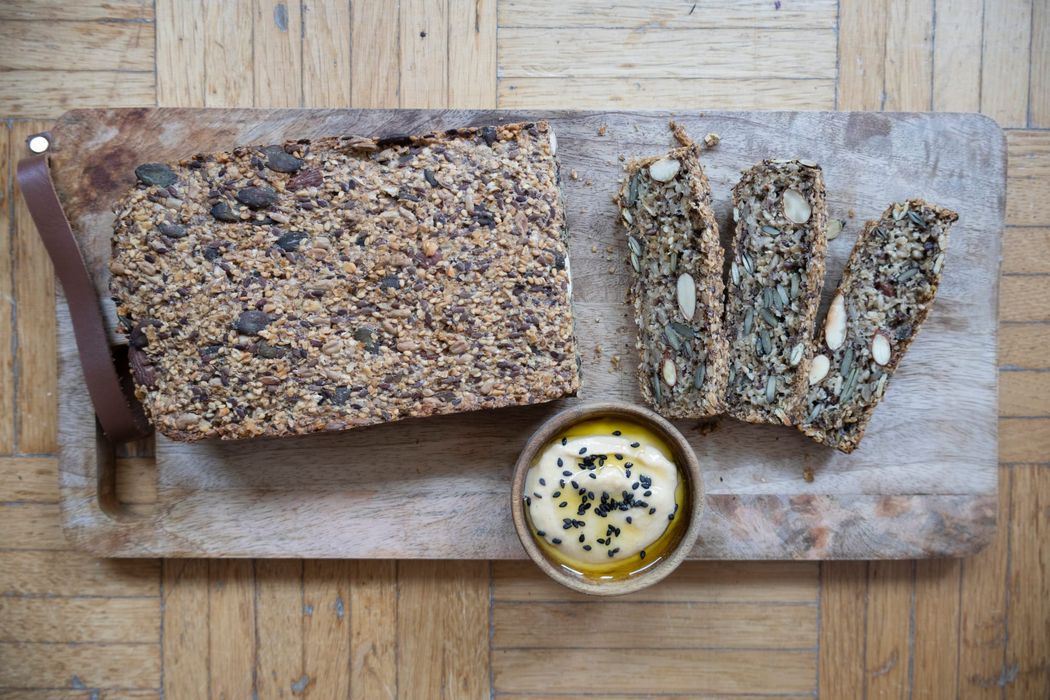 Teilweise aufgeschnittenes Saatenbrot auf Holzbrett, dazu ein Schälchen mit Hummus
