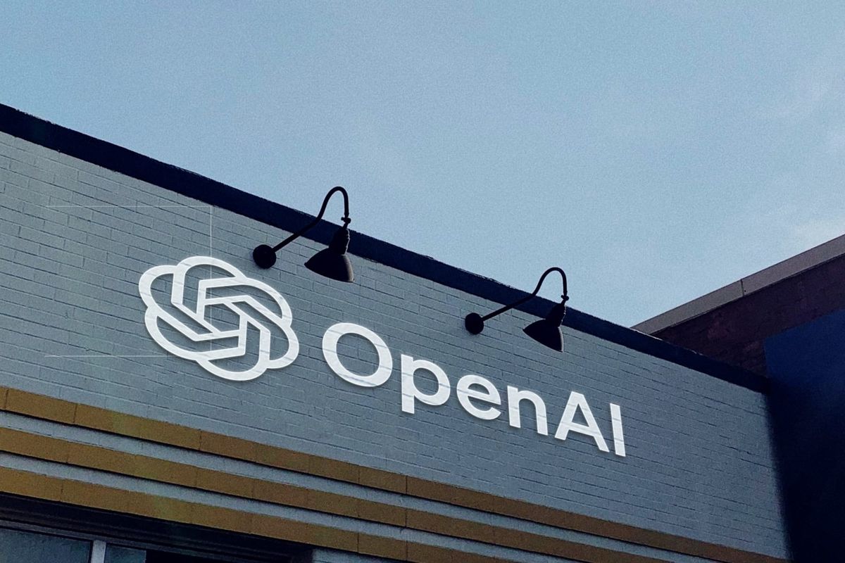 A gray brick wall with the OpenAI logo and wordmark painted on it